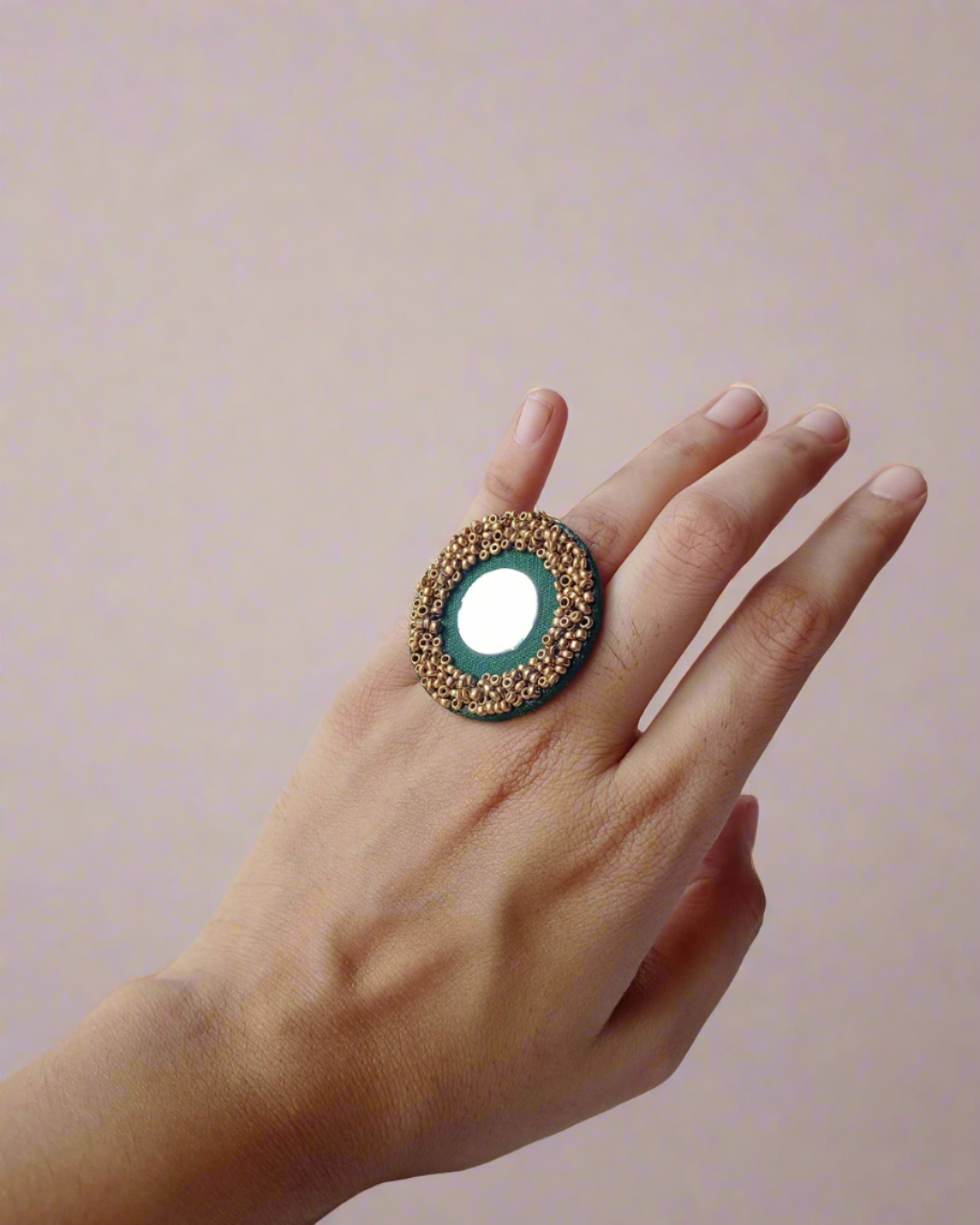 Hand wearing dark green round finger ring with mirror and golden beads border on white backdrop