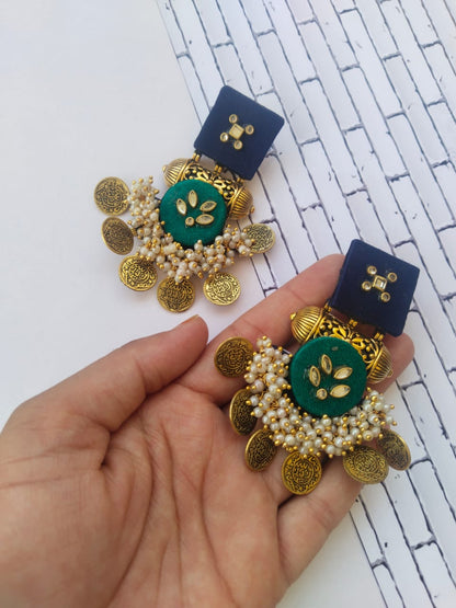 Blue and dark green earrings with golden tabiz, coins and white beads on a palm 