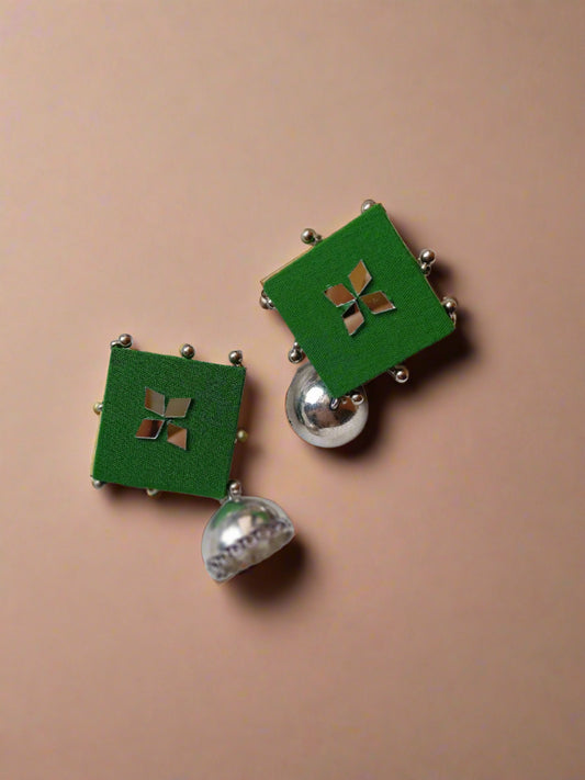 Square green jhumka with silver charm at bottom on white backdrop with an open book