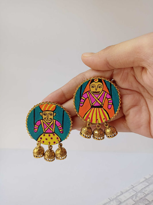 Hand holding round earrings with rajasthani handpainted gudda guddi earrings on white backdrop