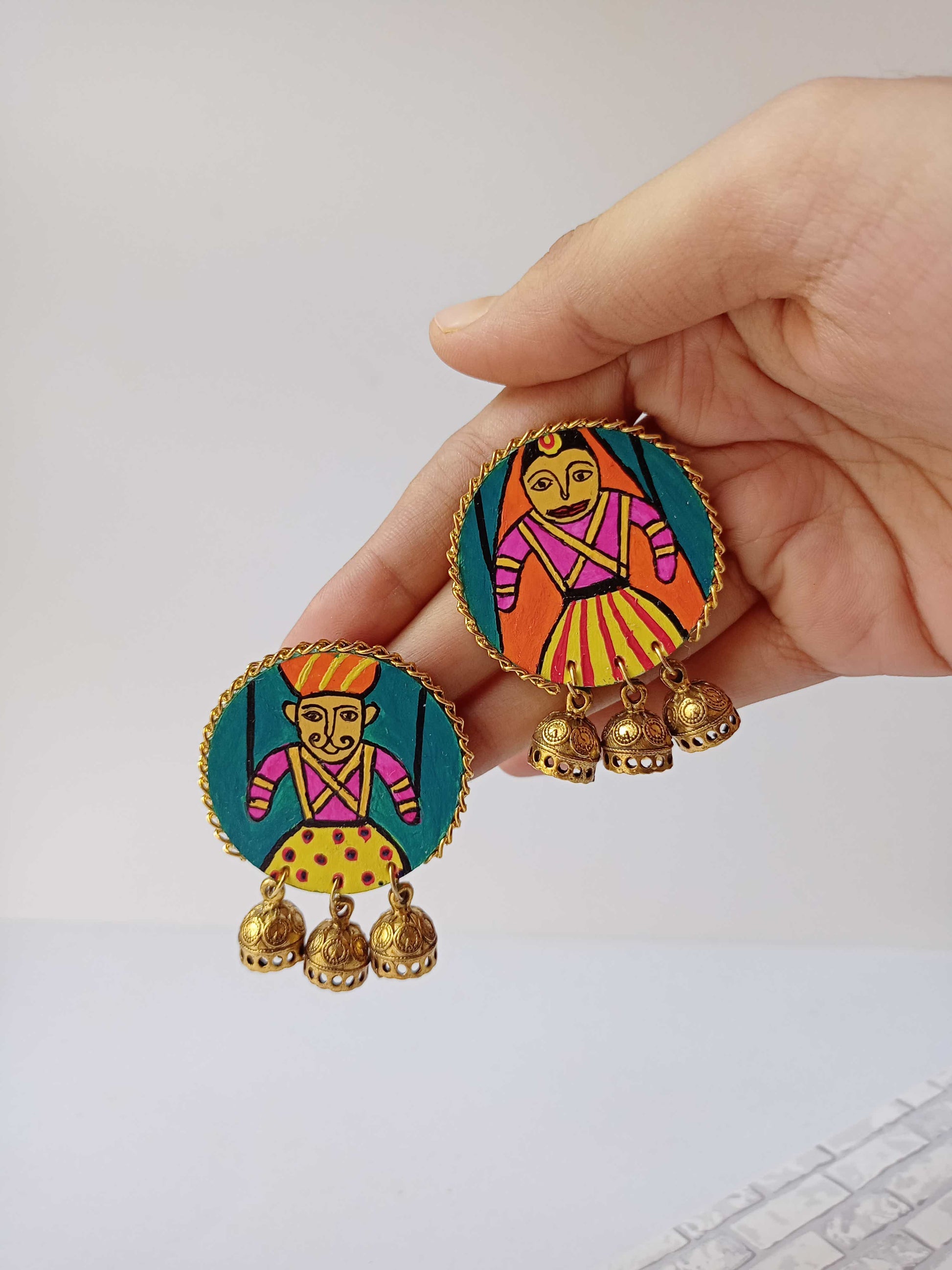 Hand holding round earrings with rajasthani handpainted gudda guddi earrings on white backdrop