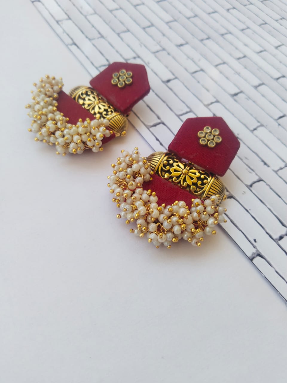 Maroon jhumka earrings with white beads and golden tabiz on white backdrop