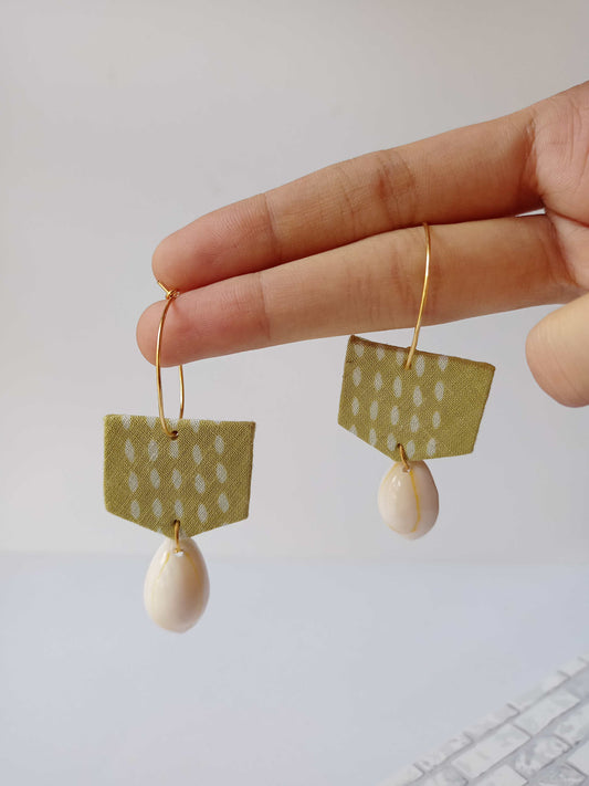 Palm holding light green hoops earrings with white sea shell at bottom on white backdrop