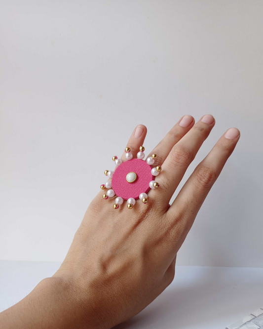 Hand wearing pink round finger ring with white pearls and beads on white backdrop