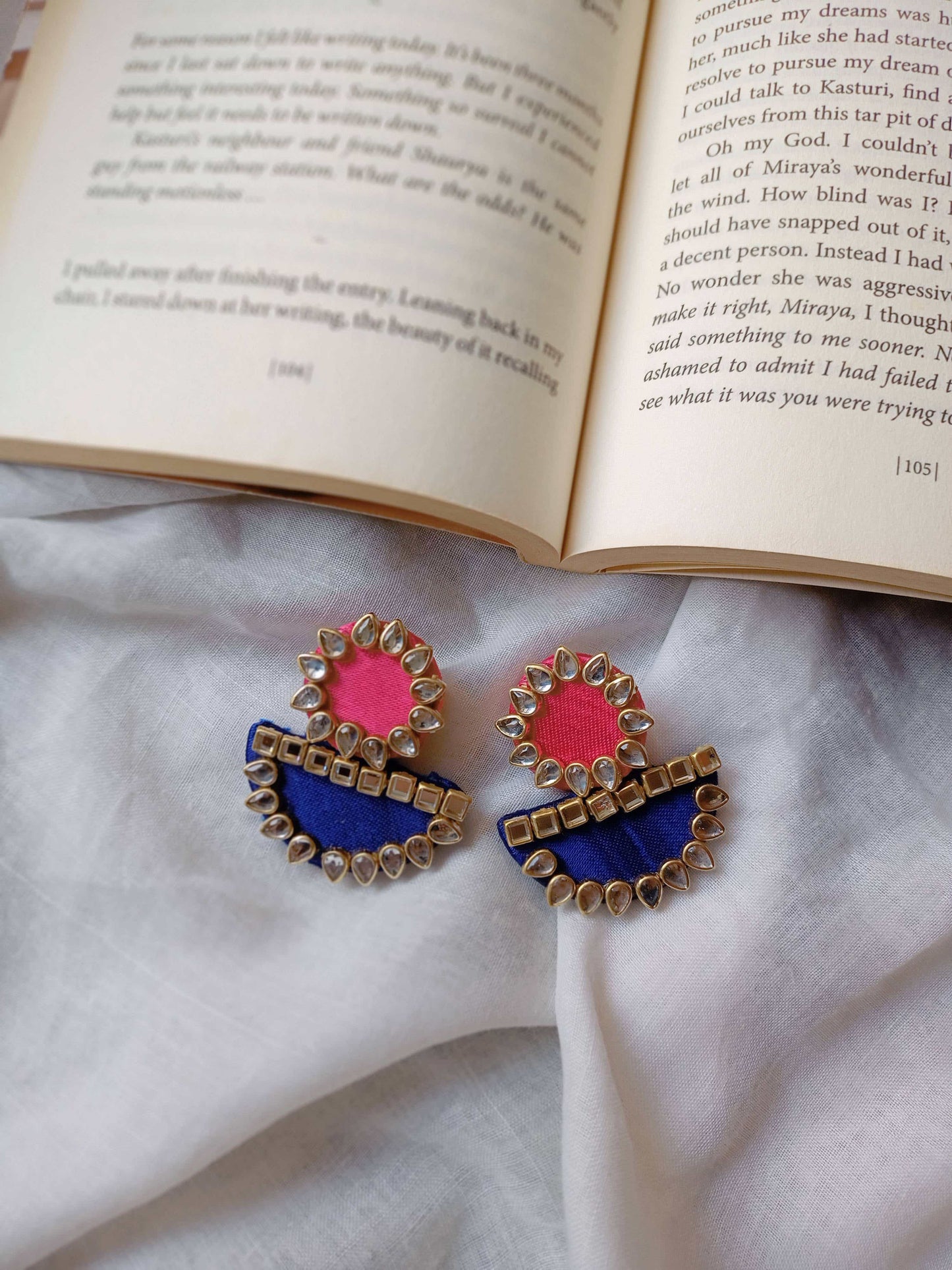 Pink and blue round and semi circle earrings with kundan border kept on open book backdrop