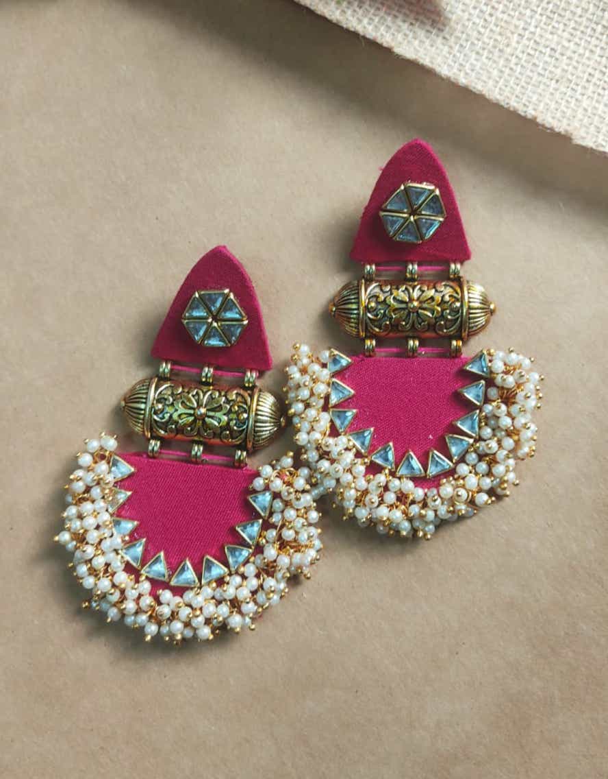 Pink jhumka earrings wit white golden beads, golden tabiz and kundan on brown backdrop