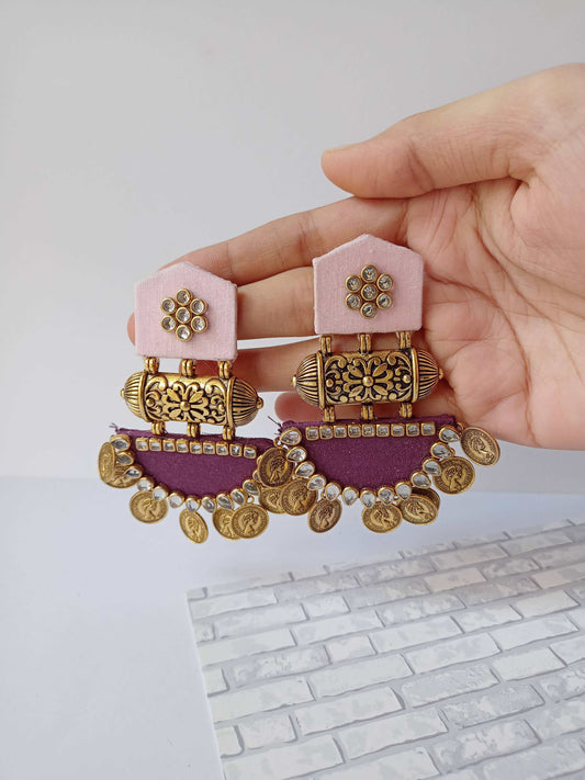 Hand holding light and dark purple jhumka earrings with golden coins and tabiz on white backdrop
