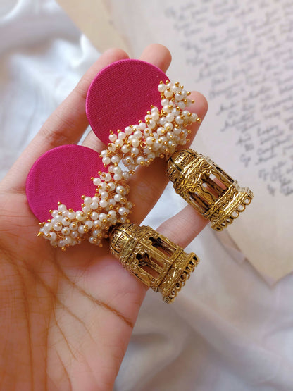 Hand holding Pink jhumka errings with golden bottom on white backdrop with open book on the right