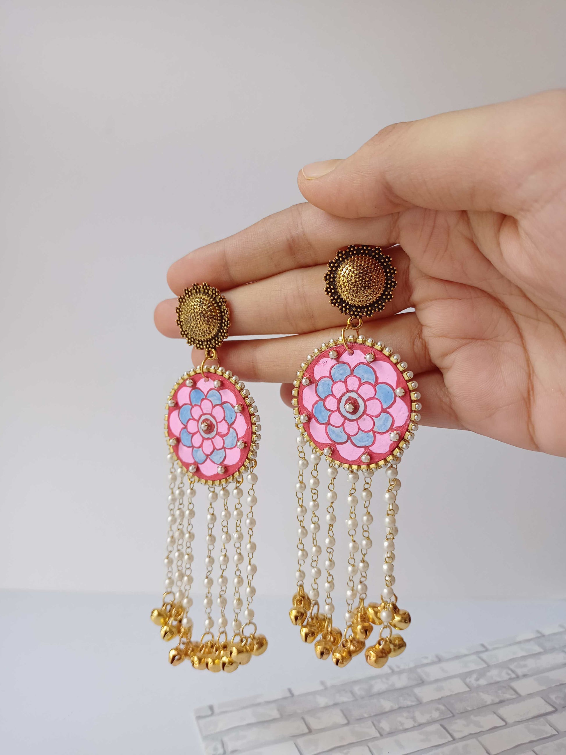 Palm holding pink mandala art round earrings with golden latkan and ghungroo at the bottom