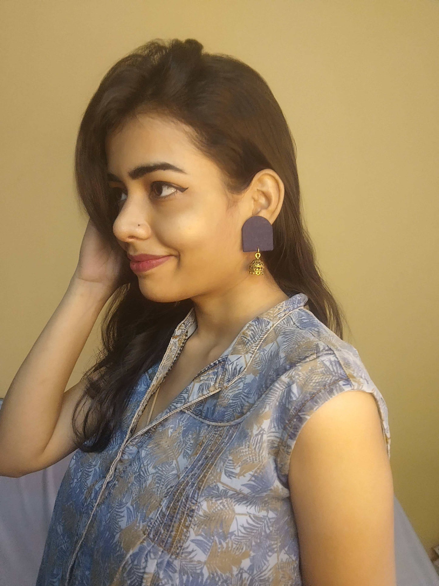 Indian girl posing with left profile wearing blue outfit with blue earrings on yellow backdrop