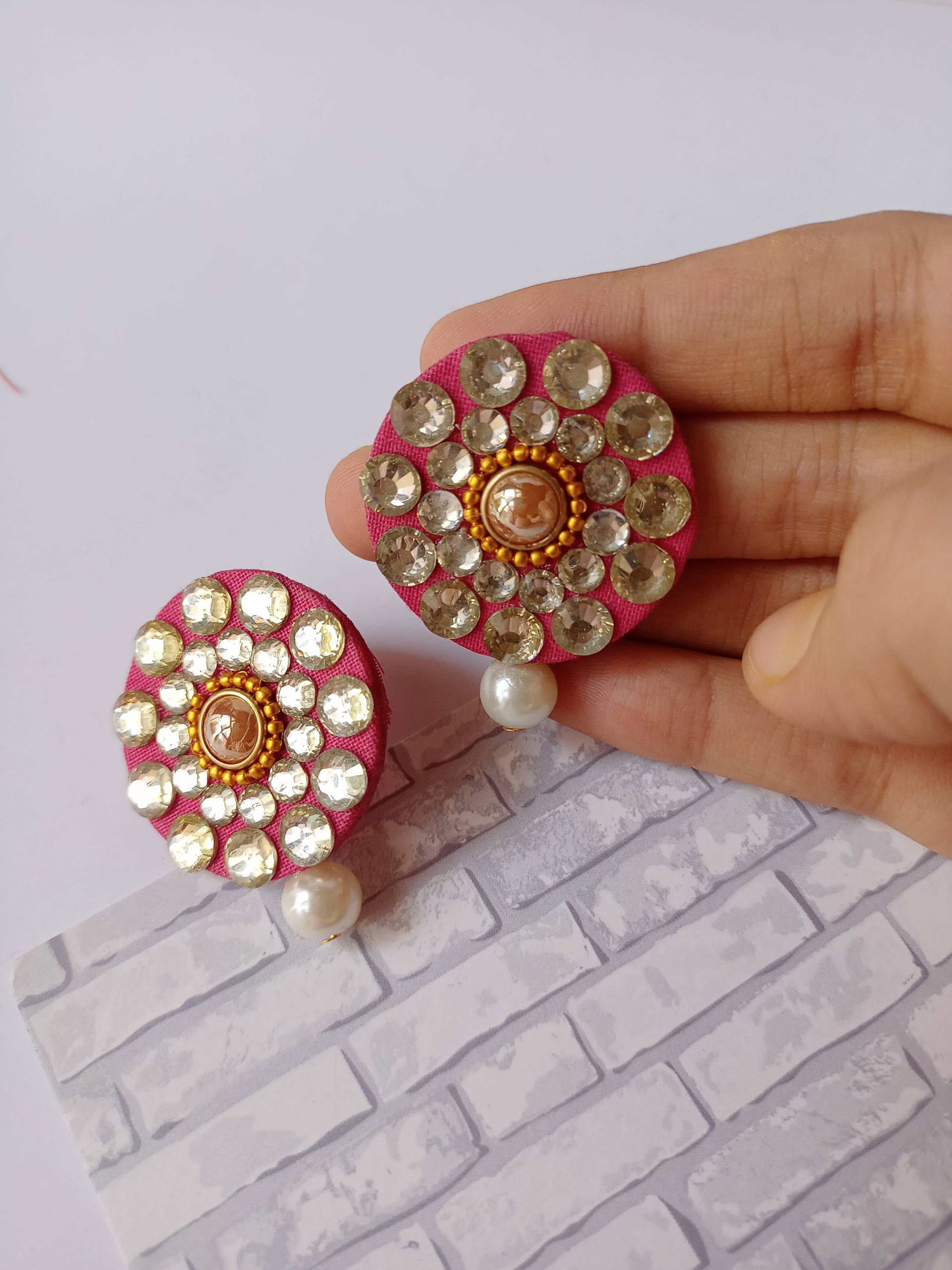 Palm holding round studs earrings with kundan and white pearl on white backdrop