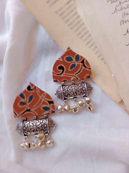 Red printed triangular shaped earrings with silver ghungroos on white backdrop