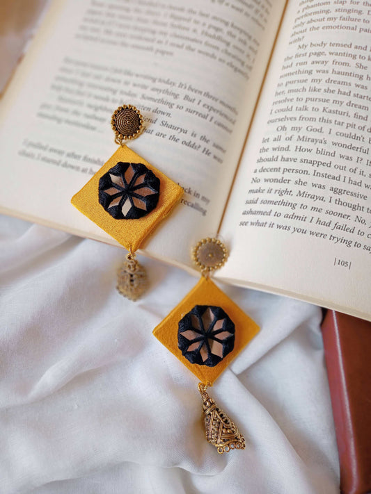 Yellow inverted square shape earrings with golden jhumar and black threads on top on white backdrop