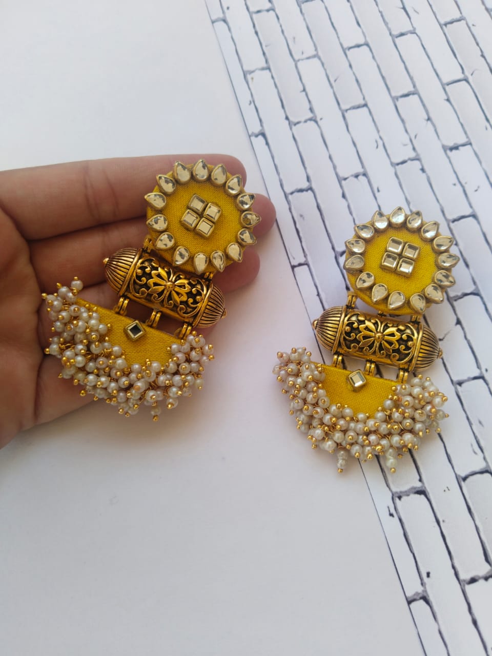 Bright lemon yellow jhumka earrings with kundan work, golden tabiz and white beads on white backdrop