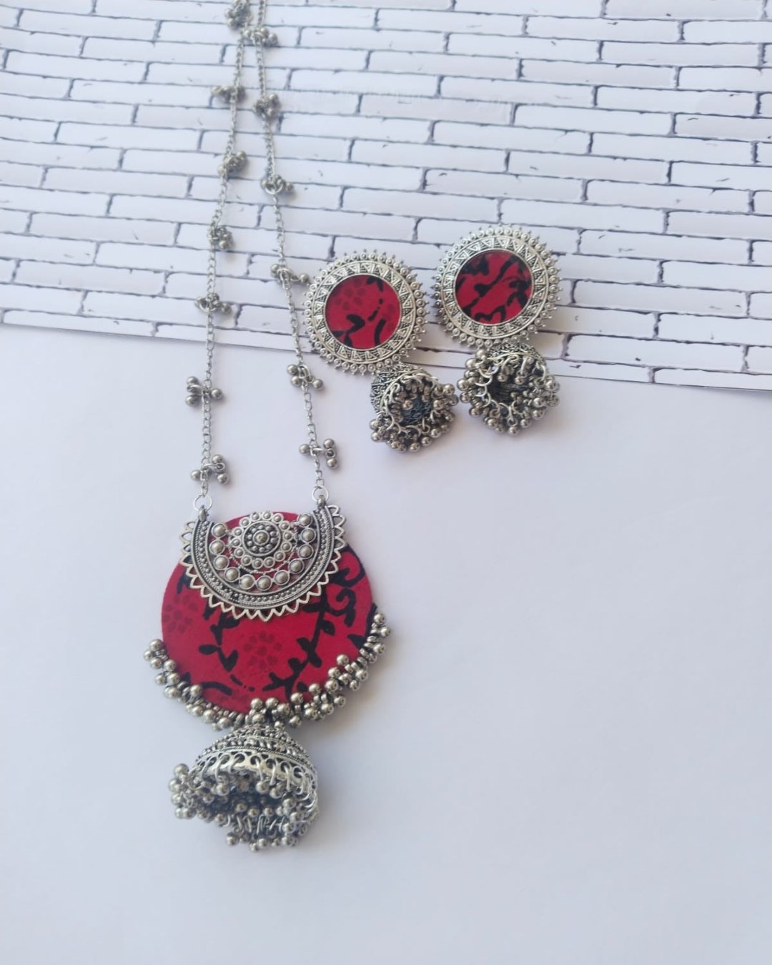 Red printed locket with silver charms and beads and silver chain with matching earrings on white backdrop