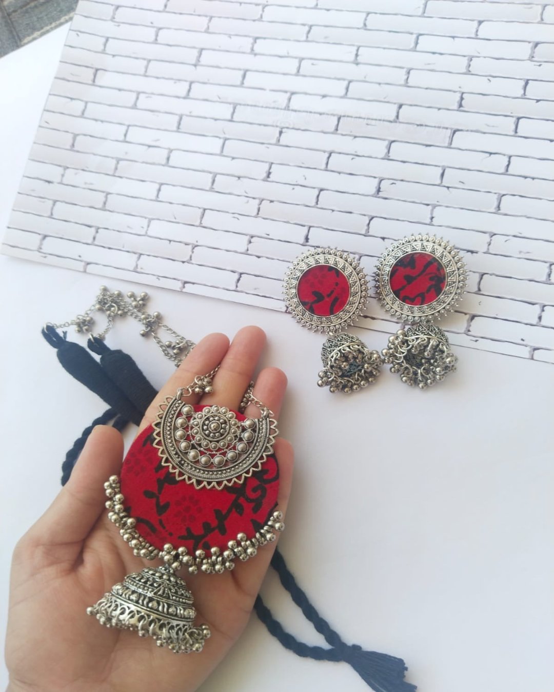 Palm holding Red printed locket with silver charms and beads and silver chain with matching earrings on white backdrop