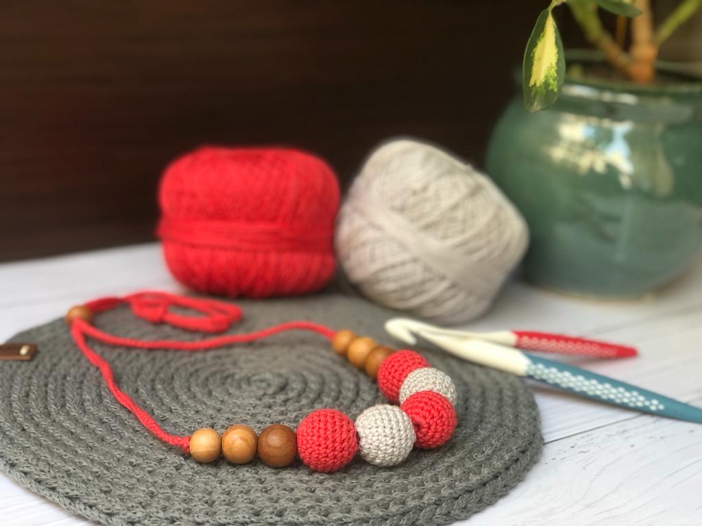 Red and white crochet beaded necklace with grey crochet base and wool in backdrop
