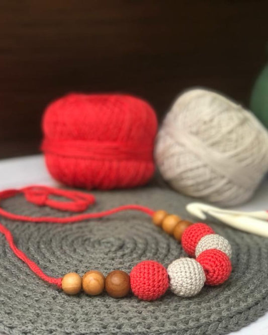 Red and white crochet beaded necklace with grey crochet base and wool in backdrop