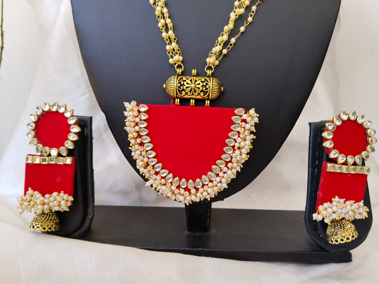 Black necklace and earrings stand with red necklace and earrings with golden beads details