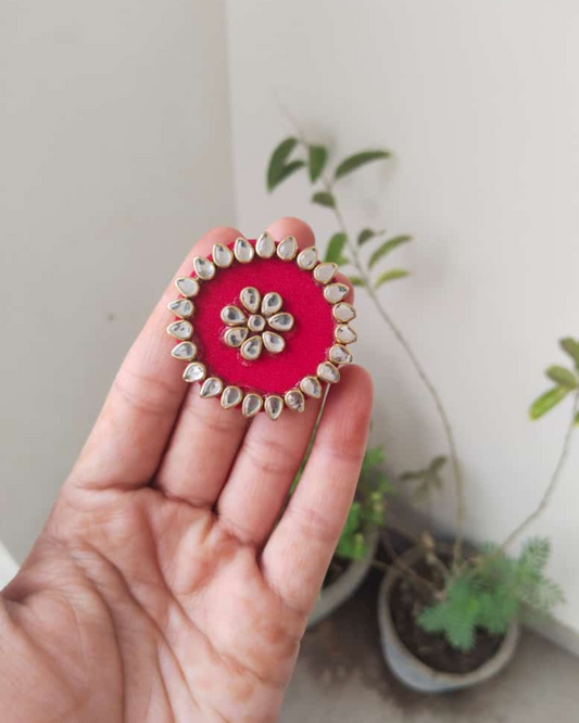 Palm wearing red round finger ring with kundan border on white backdrop