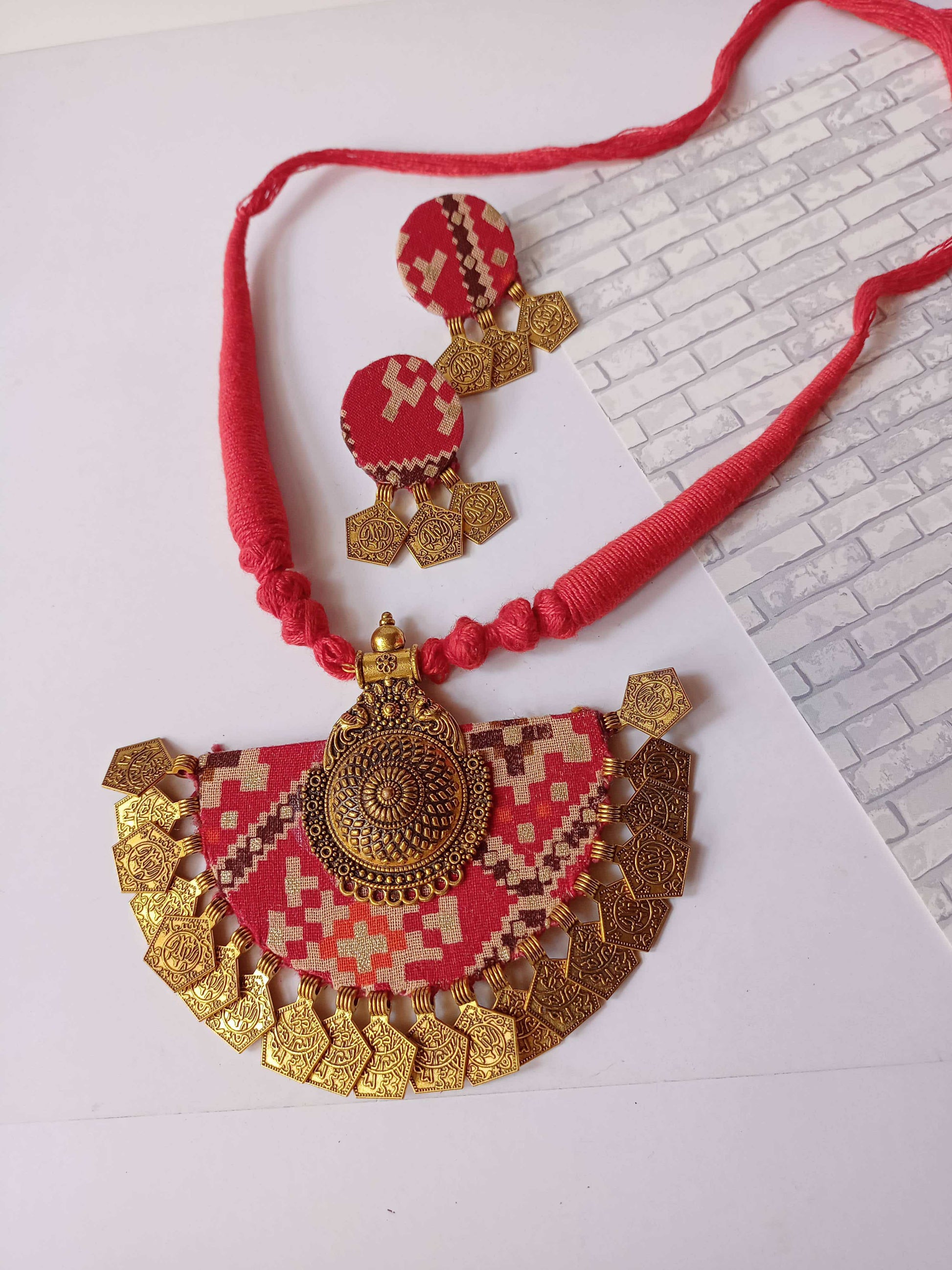 Red bandhani printed necklace with golden coins and charm and matching earrings on white backdrop