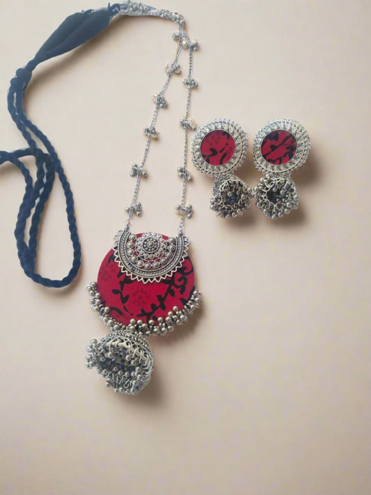 Red printed locket with silver charms and beads and silver chain with matching earrings on white backdrop