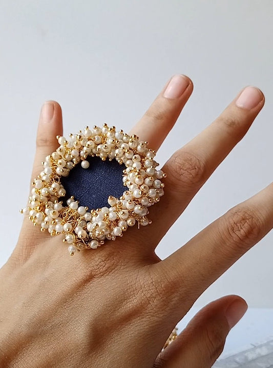Hand wearing navy blue finger ring with white beads on white backdrop