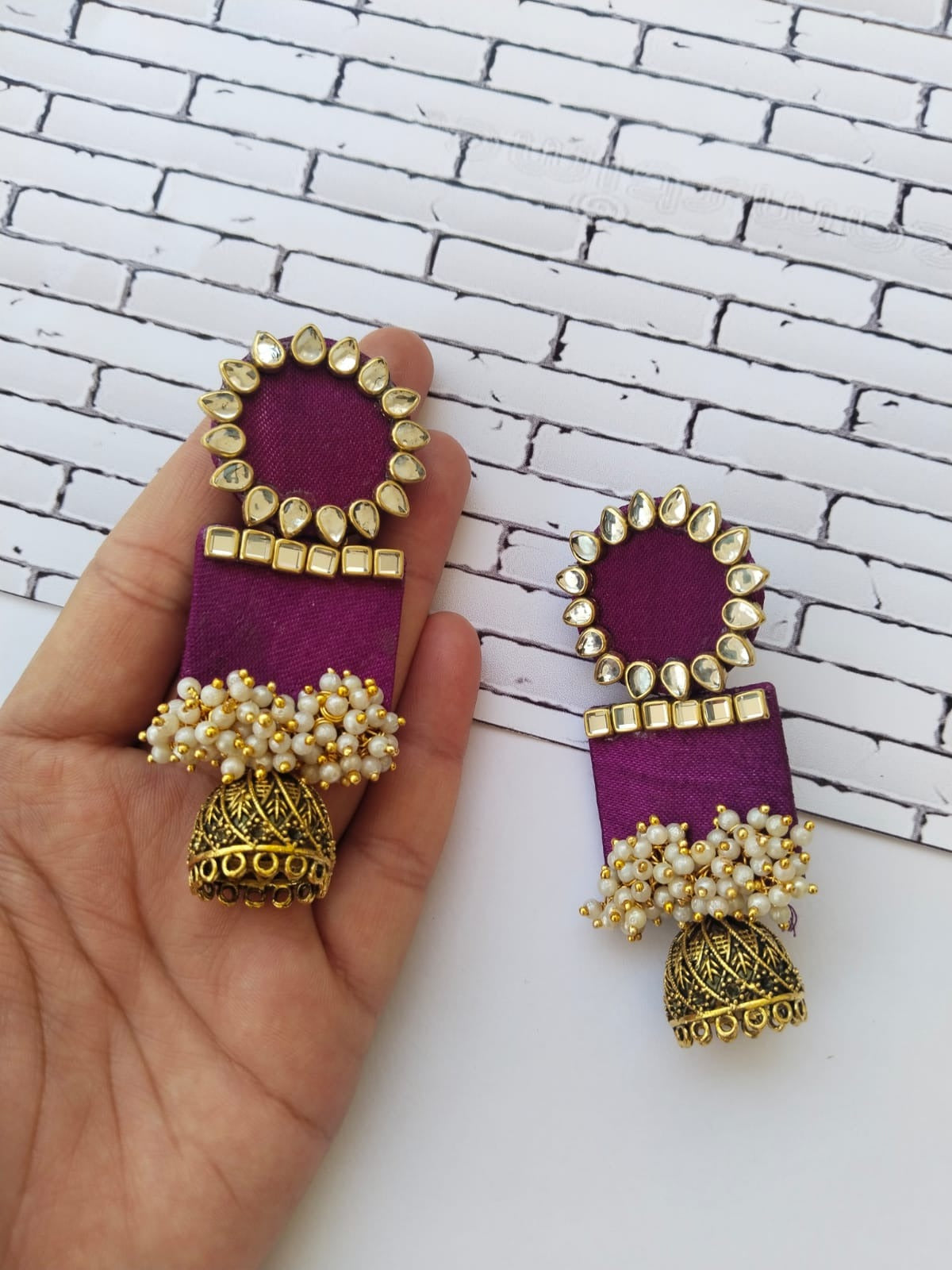 Palm holding Wine purple rectangular jhumka with white and golden beads on white grey backdrop