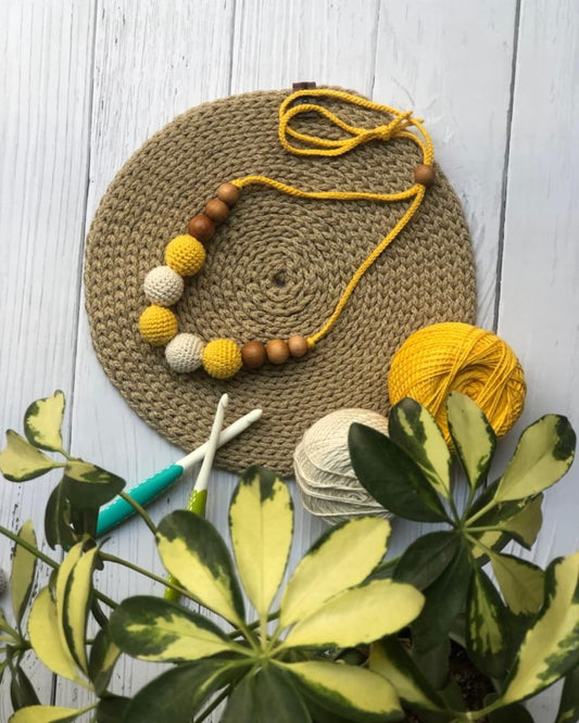 Yellow and white crochet round necklace on brown crochet base with threads in backdrop