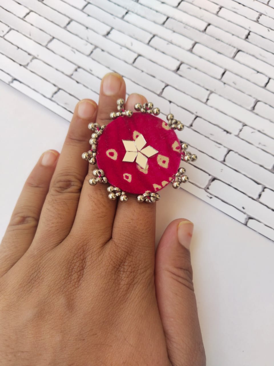 Hand wearing round red bandhani print finger ring with mirrors and ghungroo on white backdrop